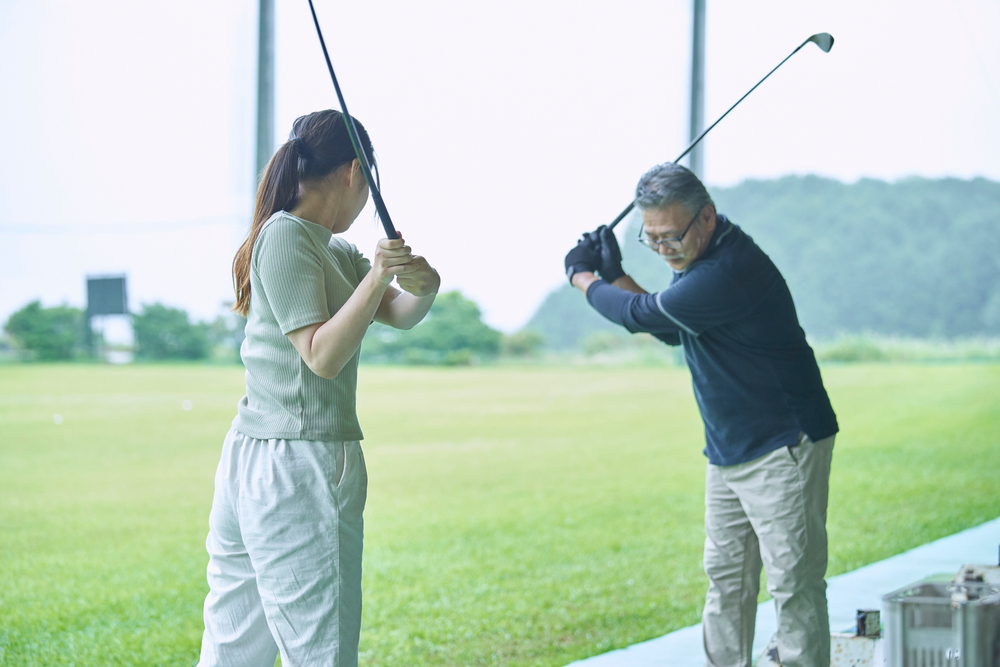 Golf instructor demonstrating swing technique to a student at an outdoor driving range